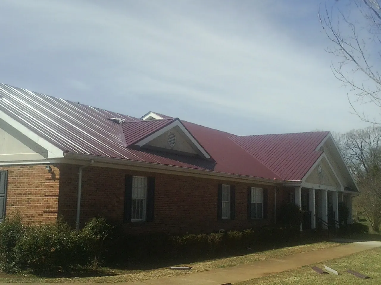 Red metal roof with gabled entries on a long brick building, from a Hail Damage Roof Repair job in Cantonment
