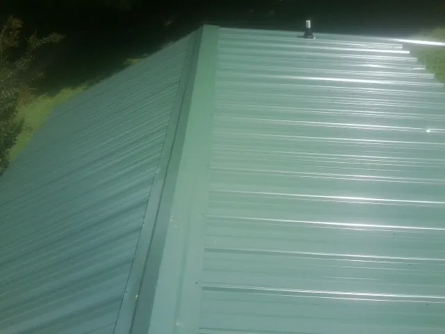 New green metal panels meeting at the ridge of a roof — Flat Roof Repair work by our crew in Cantonment