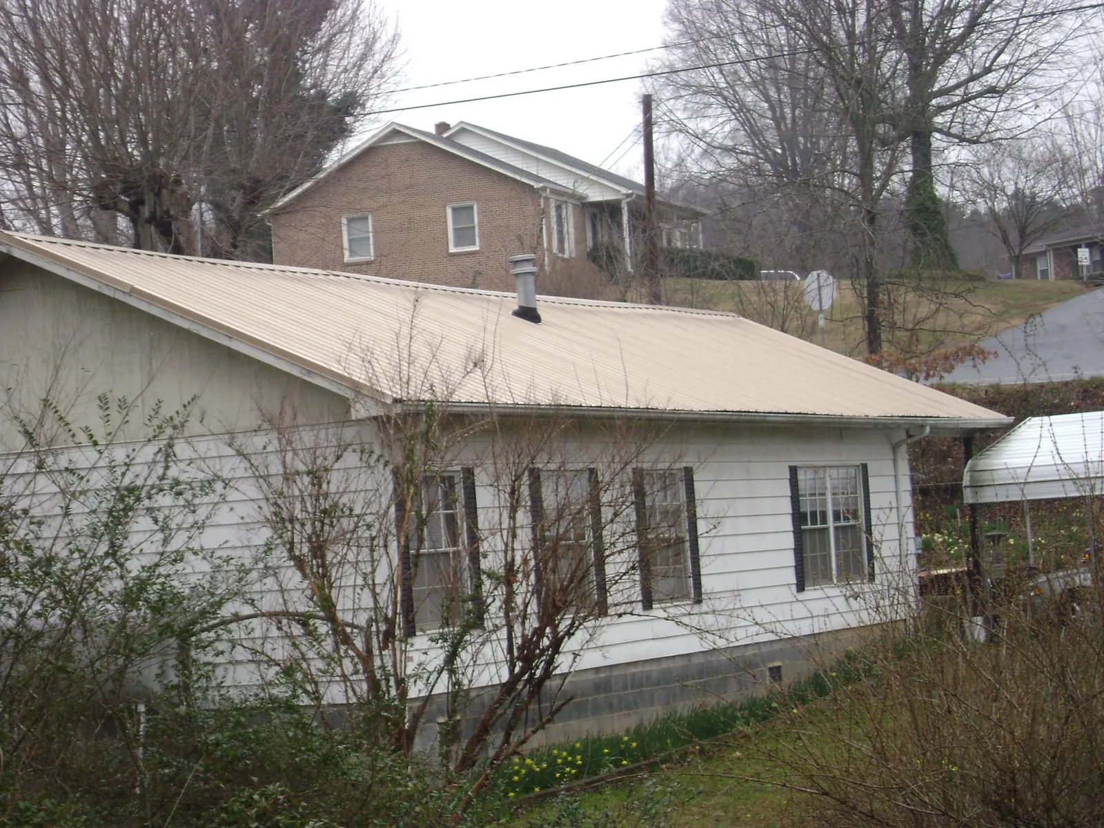 Tan metal roof on a white sided house set into a hillside — Commercial Roofing by Roofing Brothers in Cantonment
